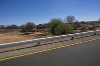 a view of a bridge from the side of a bus window, looking out to a dirt field with a rail road