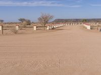 a dirt road and fence in a large desert area with houses on it and no cars on the road