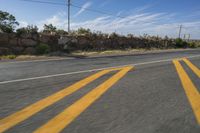 a highway with two yellow stripe lines on the road and a rock wall behind it