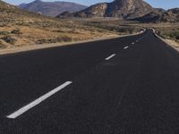 the long empty road leads into the desert with sparse trees and tall mountains in the background