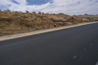 a guy riding a motorcycle down a highway in the desert with mountains in the background