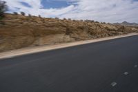 a guy riding a motorcycle down a highway in the desert with mountains in the background