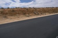 a guy riding a motorcycle down a highway in the desert with mountains in the background