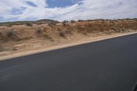 a guy riding a motorcycle down a highway in the desert with mountains in the background