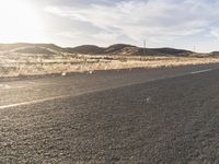 a car driving down the highway next to a hill range with rocks and dry grass