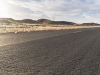 a car driving down the highway next to a hill range with rocks and dry grass