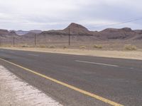 a sign near a desert road and telephone poles on an overcast day, with some hills in the background