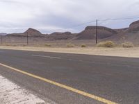 a sign near a desert road and telephone poles on an overcast day, with some hills in the background