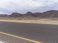 a sign near a desert road and telephone poles on an overcast day, with some hills in the background