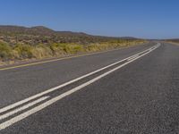 the highway has three white lines on the road that lead to two small hills in the distance