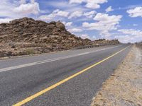 the empty street is on the rocky hill side and yellow paint shows the line of a curving road