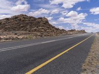 the empty street is on the rocky hill side and yellow paint shows the line of a curving road