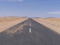 empty road near desert area with mountains in background, no people yet on it, in the distance are bushes and sparse clouds