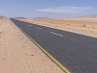 empty road near desert area with mountains in background, no people yet on it, in the distance are bushes and sparse clouds