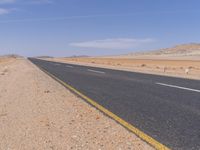 empty road near desert area with mountains in background, no people yet on it, in the distance are bushes and sparse clouds