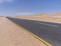 empty road near desert area with mountains in background, no people yet on it, in the distance are bushes and sparse clouds