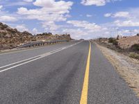 the empty street is on the rocky hill side and yellow paint shows the line of a curving road