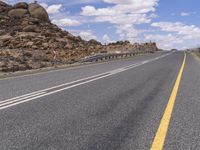 the empty street is on the rocky hill side and yellow paint shows the line of a curving road