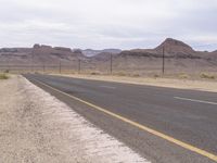 an empty highway running through the deserts with mountains in the background, and telephone poles with wires on either side