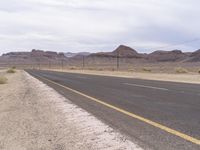an empty highway running through the deserts with mountains in the background, and telephone poles with wires on either side