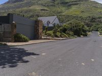 there is a house and fence in the front yard with mountains behind it and blue skies above