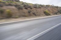 a motorcycle driving down the road in the day time and blurry background with bushes and hills