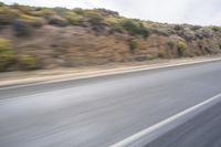 a motorcycle driving down the road in the day time and blurry background with bushes and hills