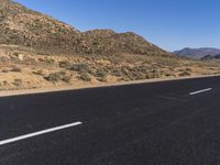 a paved road in the desert with no people on it and bushes and dirt everywhere