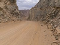 a small vehicle traveling across a barren road between some large rocks and boulders on one side