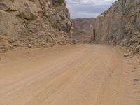 a small vehicle traveling across a barren road between some large rocks and boulders on one side