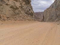 a small vehicle traveling across a barren road between some large rocks and boulders on one side