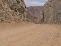 a small vehicle traveling across a barren road between some large rocks and boulders on one side