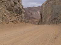 a small vehicle traveling across a barren road between some large rocks and boulders on one side