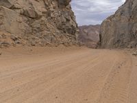 a small vehicle traveling across a barren road between some large rocks and boulders on one side