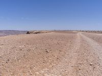 a road that is made from rocks in a desert area with mountains and a blue sky