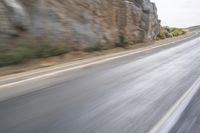 motorcycle rider turning right on empty highway surrounded by rocks and mountains in motion blurry