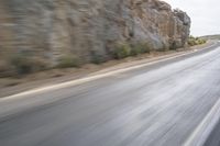 motorcycle rider turning right on empty highway surrounded by rocks and mountains in motion blurry