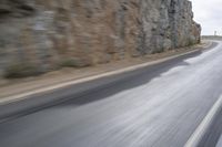 motorcycle rider turning right on empty highway surrounded by rocks and mountains in motion blurry