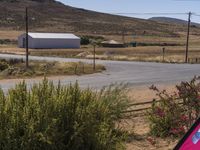 an empty road leading up a hill to a large white building and mountains in the distance