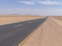 empty road near desert area with mountains in background, no people yet on it, in the distance are bushes and sparse clouds