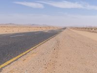 empty road near desert area with mountains in background, no people yet on it, in the distance are bushes and sparse clouds