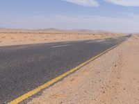 empty road near desert area with mountains in background, no people yet on it, in the distance are bushes and sparse clouds