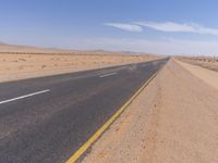 empty road near desert area with mountains in background, no people yet on it, in the distance are bushes and sparse clouds