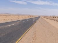 empty road near desert area with mountains in background, no people yet on it, in the distance are bushes and sparse clouds