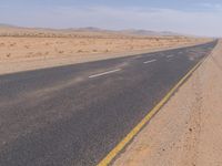 empty road near desert area with mountains in background, no people yet on it, in the distance are bushes and sparse clouds