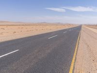 empty road near desert area with mountains in background, no people yet on it, in the distance are bushes and sparse clouds