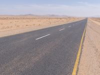 empty road near desert area with mountains in background, no people yet on it, in the distance are bushes and sparse clouds