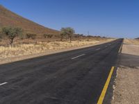 an empty road on the desert near a hill in the desert in the usa and a stop sign is in view