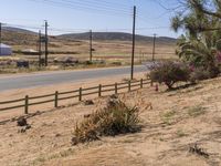 a view of an open road with telephone poles and some dirt grass and bushes around