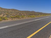 an empty road with no traffic or cars on it in the desert area, and hills in the distance